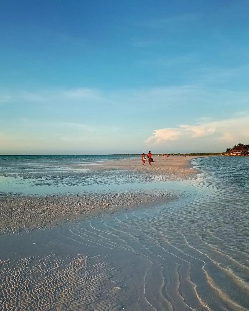 Couple walking along the shallow turquoise shores of Holbox at golden hour