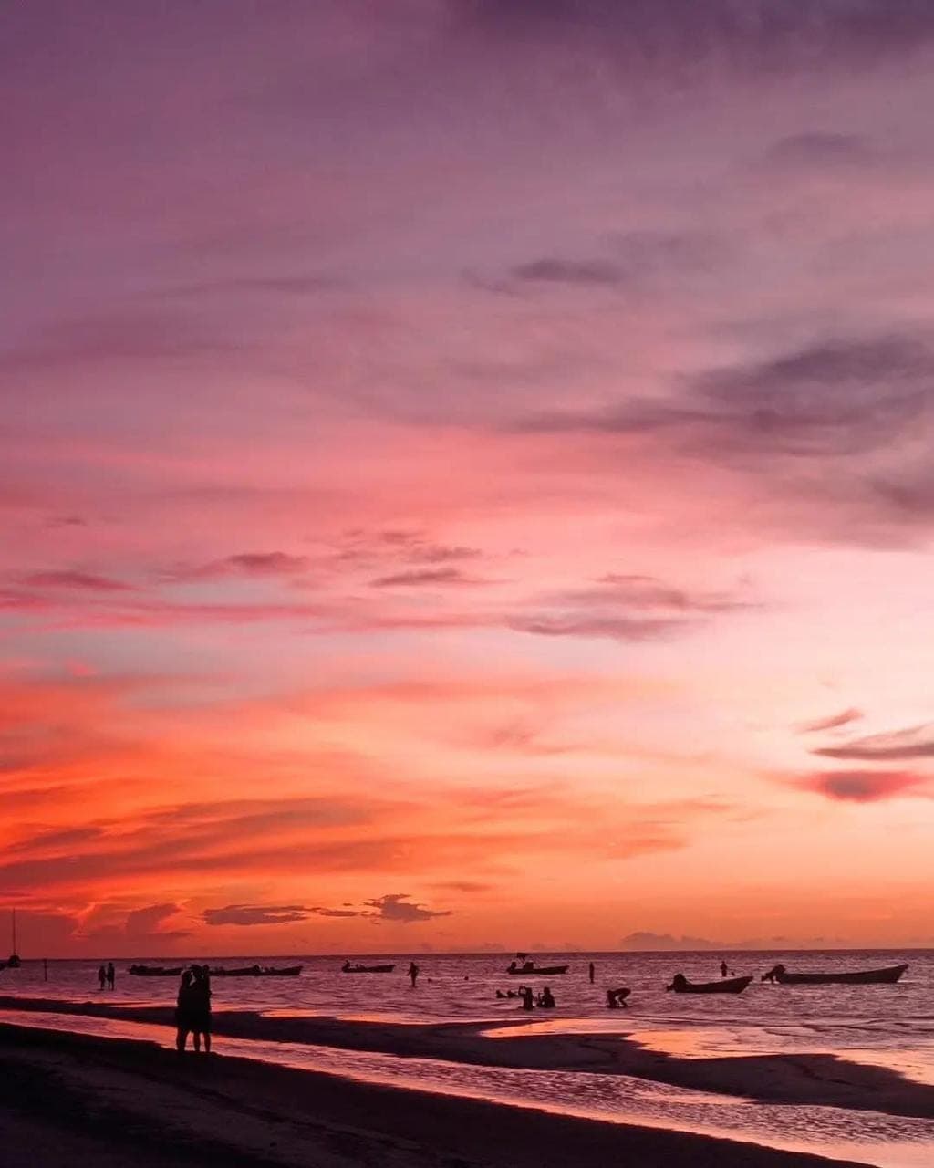Vivid magenta and pink sunset over Holbox beach with fishing boat silhouettes