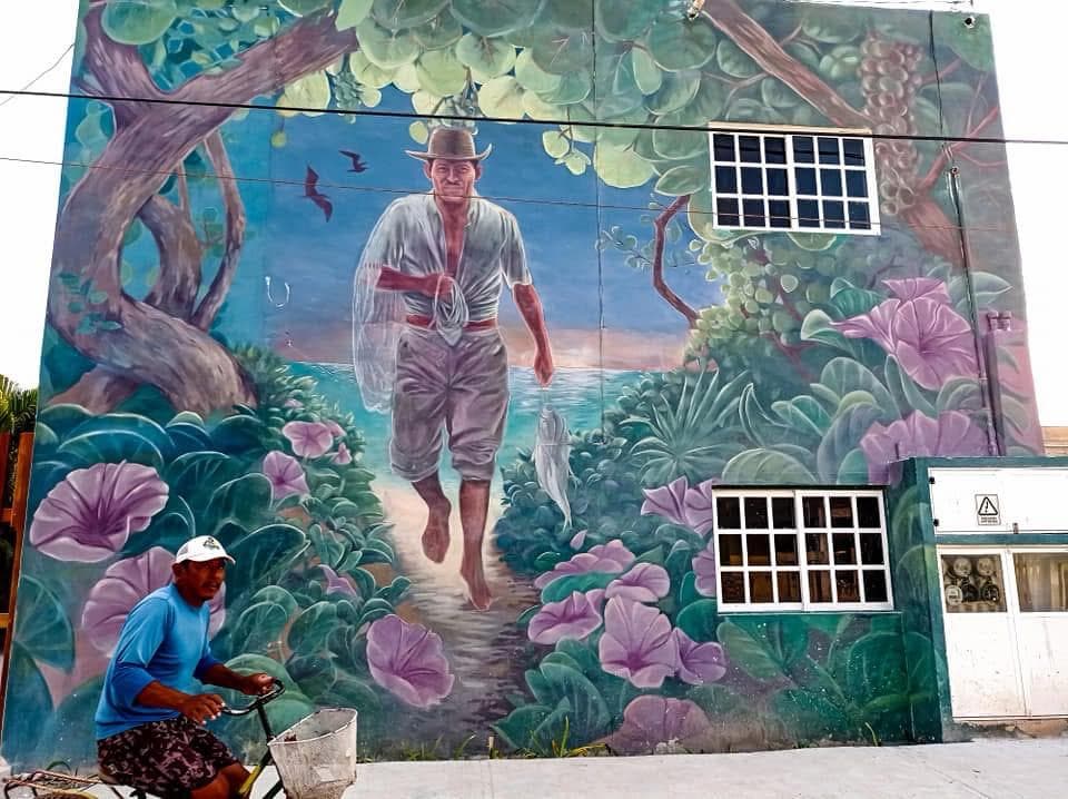 Mural of a man walking through tropical flowers on a Holbox building